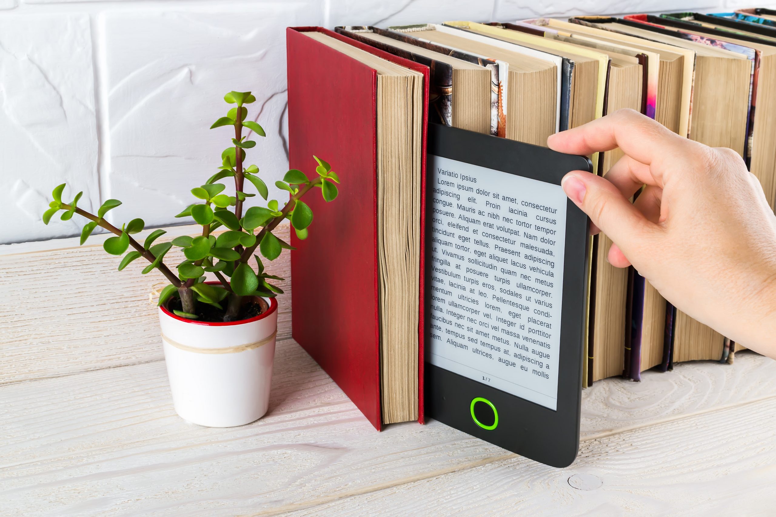 Hand nimmt einen E-Reader aus einem Regal mit gedruckten Büchern und kleinen Topfpflanzen.